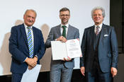 Peter Lange (l.) und Dr.-Ing. Lothar Wilhelmy (r.) verleihen den Klung-Wilhelmy-Wissenschafts-Preis 2019 an Prof. Dr. Titus Neupert (m.).